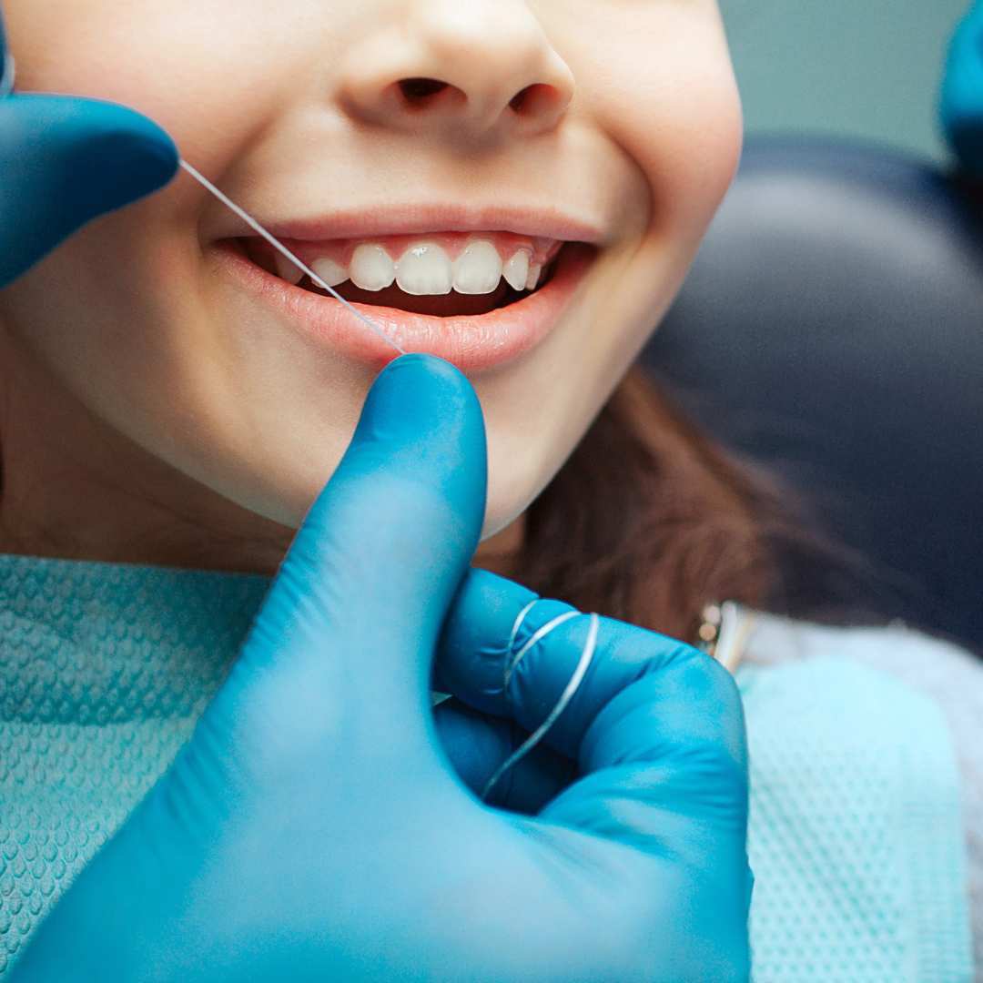 Gloved hands hold a piece of floss by a child's teeth. The child is sitting in a dentist's chair.