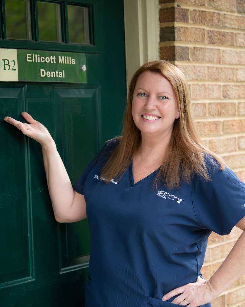 Dr. Kimberly Ford standing in front of a green door gesturing to a plaque on the door that reads "B2, Ellicott Mills Dental"